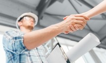builder with blueprint shaking partner hand